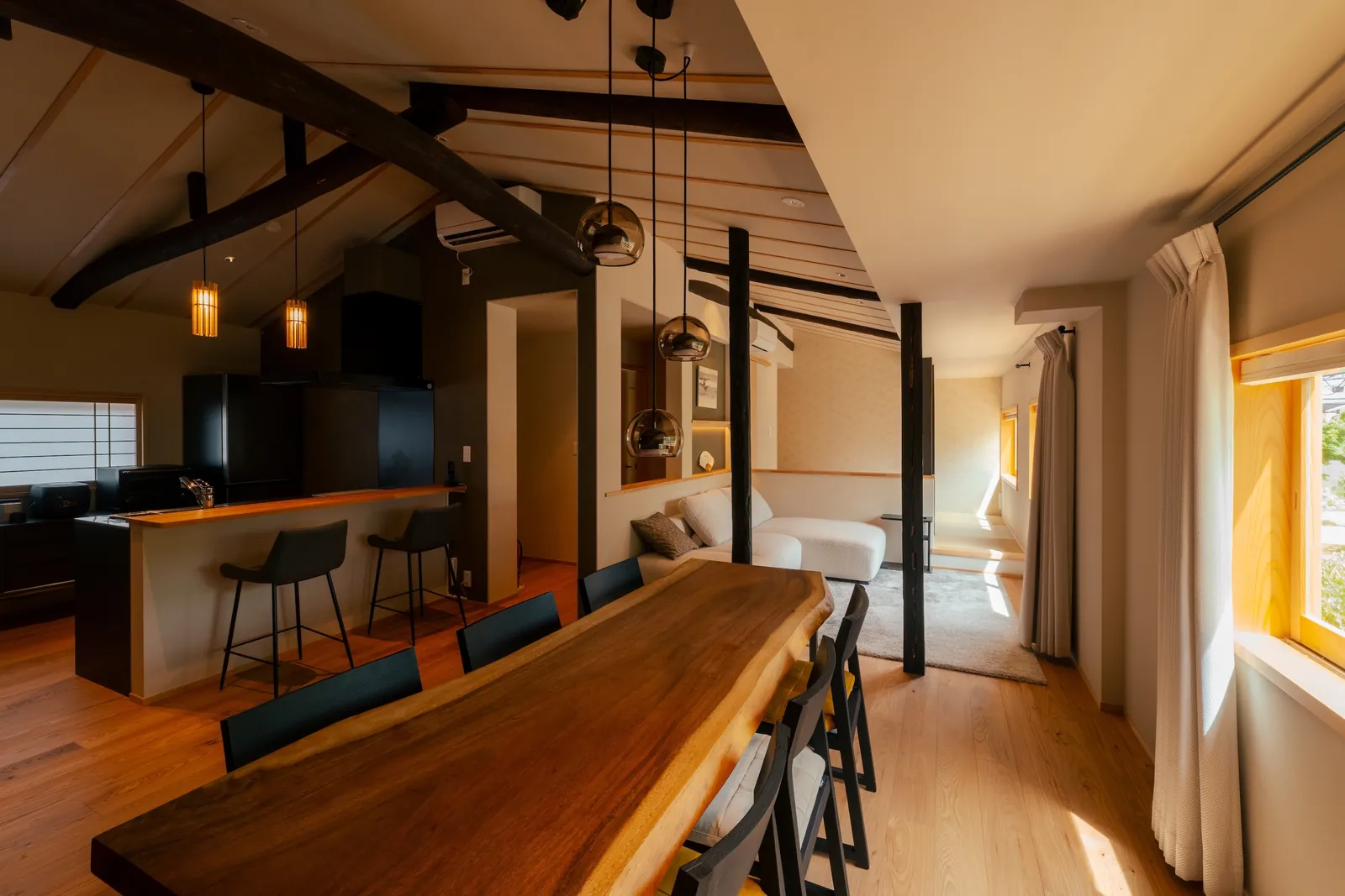 梁とキッチンを望む一棟貸し町家のリビング・ダイニング全景 / The open-beamed living and dining space of Kou with its kitchen counter, a one-group-a-day private machiya in Kyoto