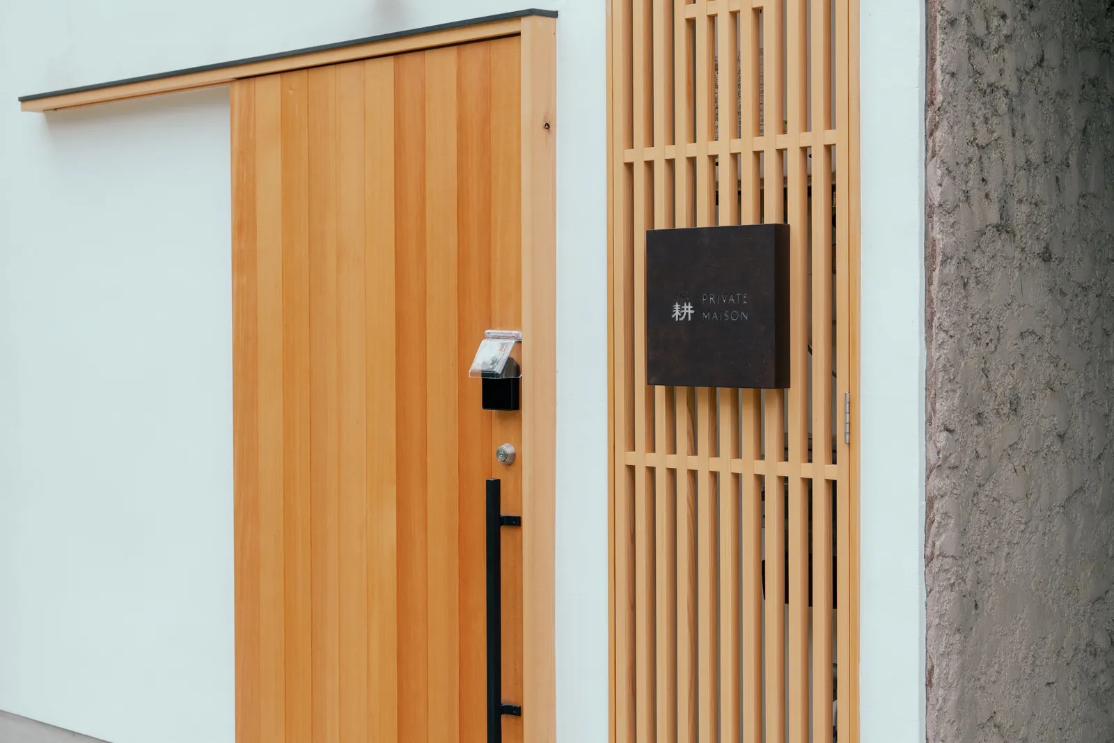木の引き戸と「耕 PRIVATE MAISON」のサインが掛かる玄関 / The wooden entrance door of Kou with its bronze nameplate