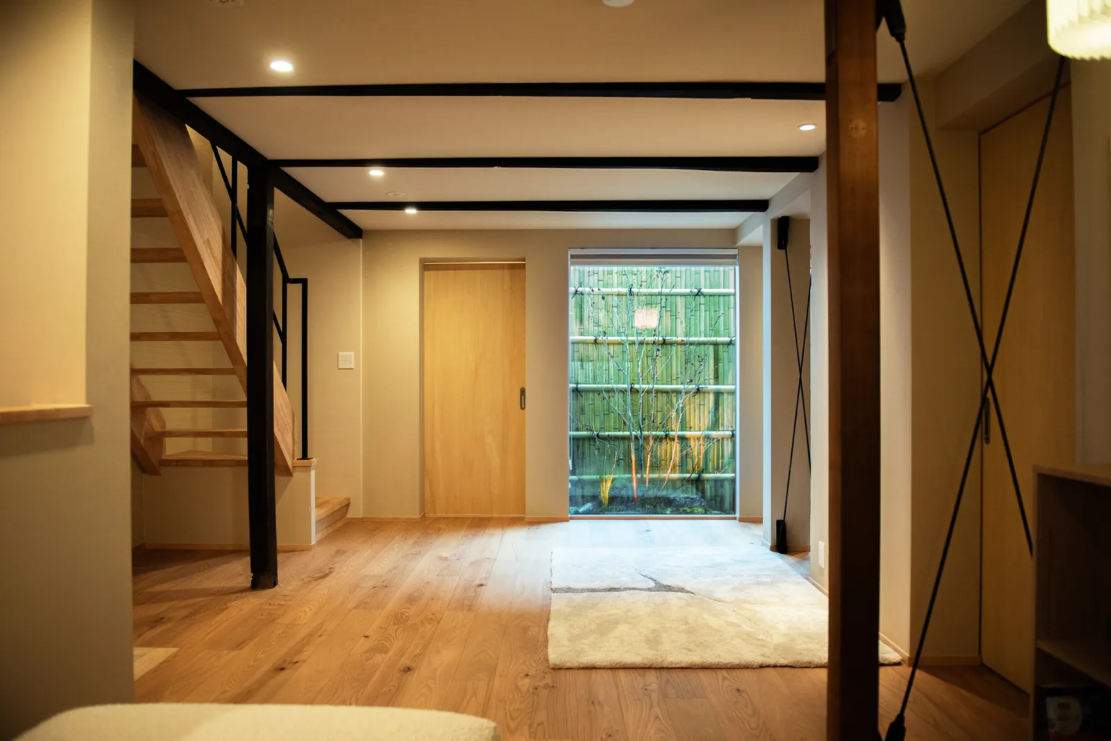 竹垣の坪庭を望む1階リビングと階段 / The first-floor living room and staircase of Kou, looking onto a bamboo-fenced courtyard garden
